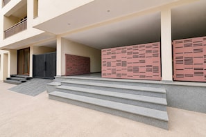 A building entrance with a set of steps leading up to a covered area, a black gate, and a red and pink patterned wall. - Classic With Balcony Townhouse Sector 52 (Gurugram)