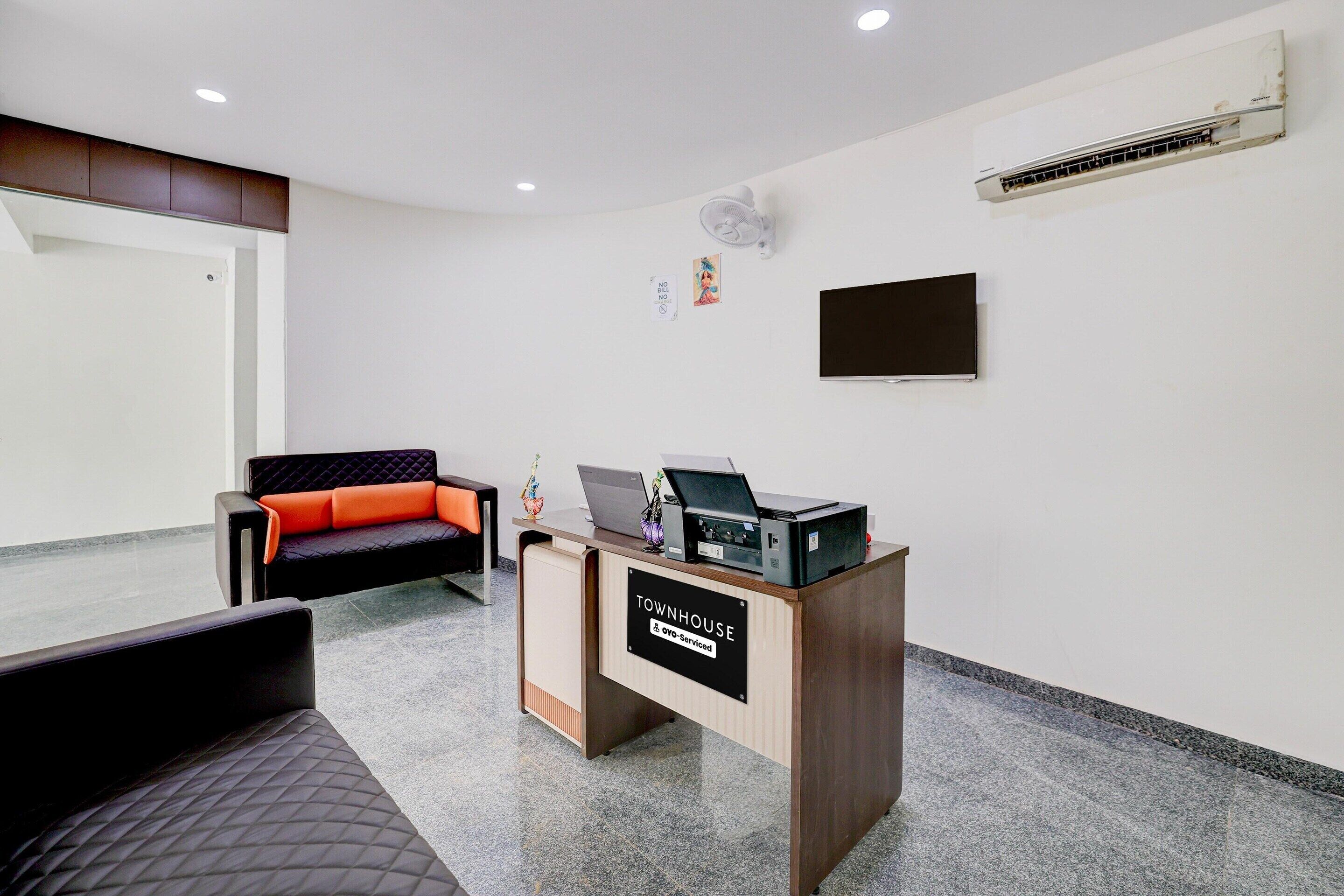 Un espace d’accueil comprenant un bureau, un canapé, un téléviseur à écran plat et un appareil de climatisation.