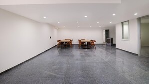 Een ruime kamer met een gepolijste betonnen vloer, een houten tafel met stoelen, een koelkast en een raam.