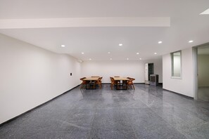 A spacious room with a polished concrete floor, a wooden table with chairs, a refrigerator, and a window. - Classic With Balcony Townhouse Sector 52 (Gurugram)