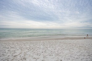 Ein Strand mit Fußspuren, die zum Wasser führen, ein Kind beim Spielen und ein bewölkter Himmel.