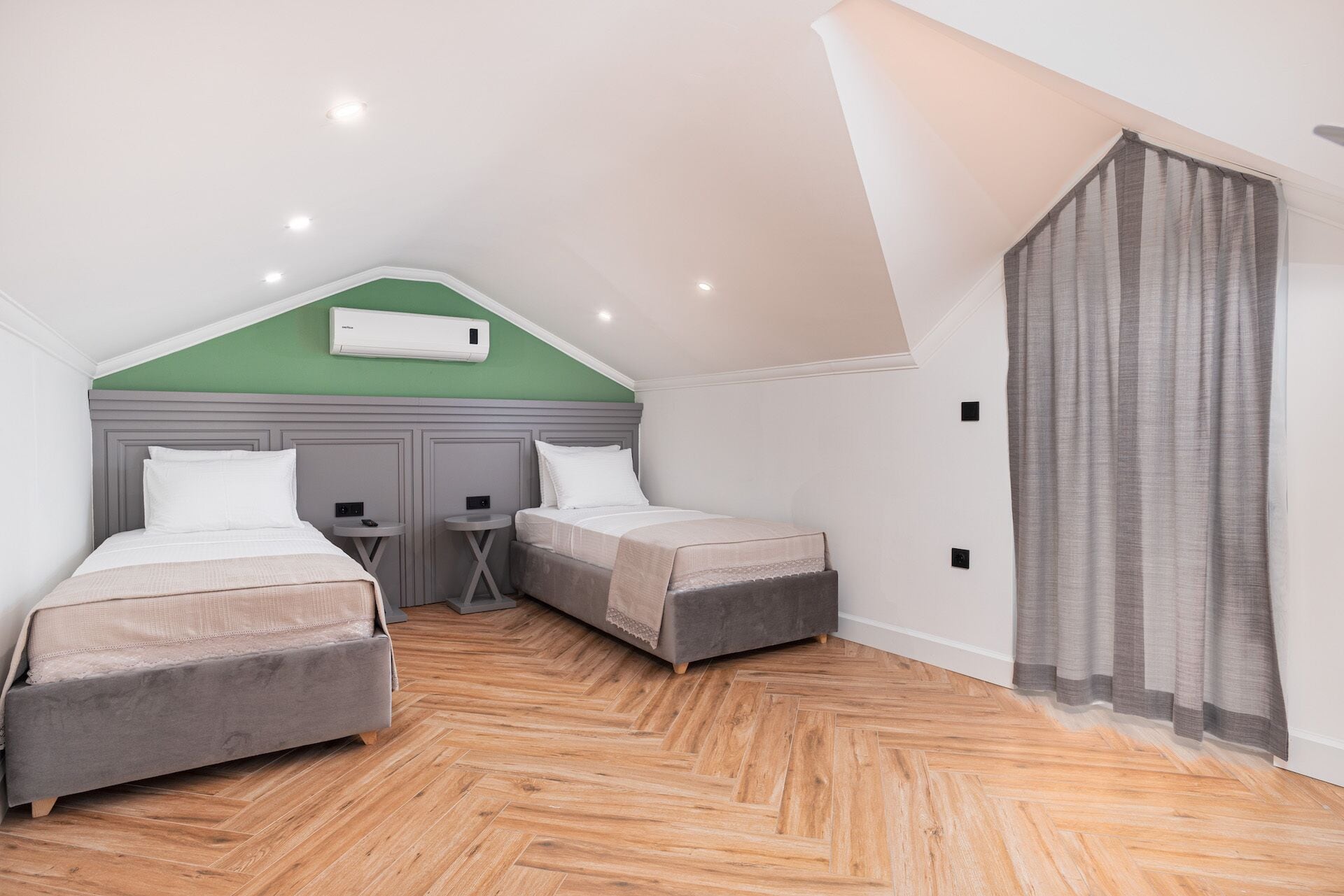 A bedroom with two beds, a small table, and a ceiling-mounted air conditioner.