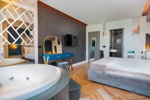 A modern bedroom with a large bed, a vanity with a mirror, a television, and a bathroom with a sink and shower.