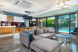 A modern living room with a sectional sofa, a small table, and a view of a swimming pool through large windows.
