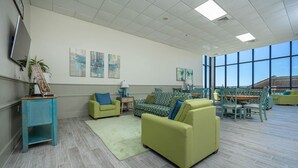 A spacious room with a large window, a green sofa, a patterned sofa, and a dining area with chairs and a table. - Phoenix I 1045 2 Bedroom Condo (Orange Beach)