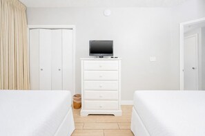 A hotel room with two beds, a white dresser with a television on top, a white door, and a light-colored floor. - Phoenix X 401 3 Bedroom Condo (Orange Beach)
