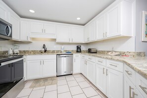 A modern kitchen with white cabinets, a stainless steel dishwasher, and a granite countertop. - Phoenix X 401 3 Bedroom Condo (Orange Beach)