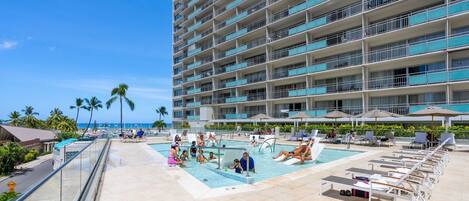 A hotel pool area with multiple levels, outdoor seating, and a view of the ocean.