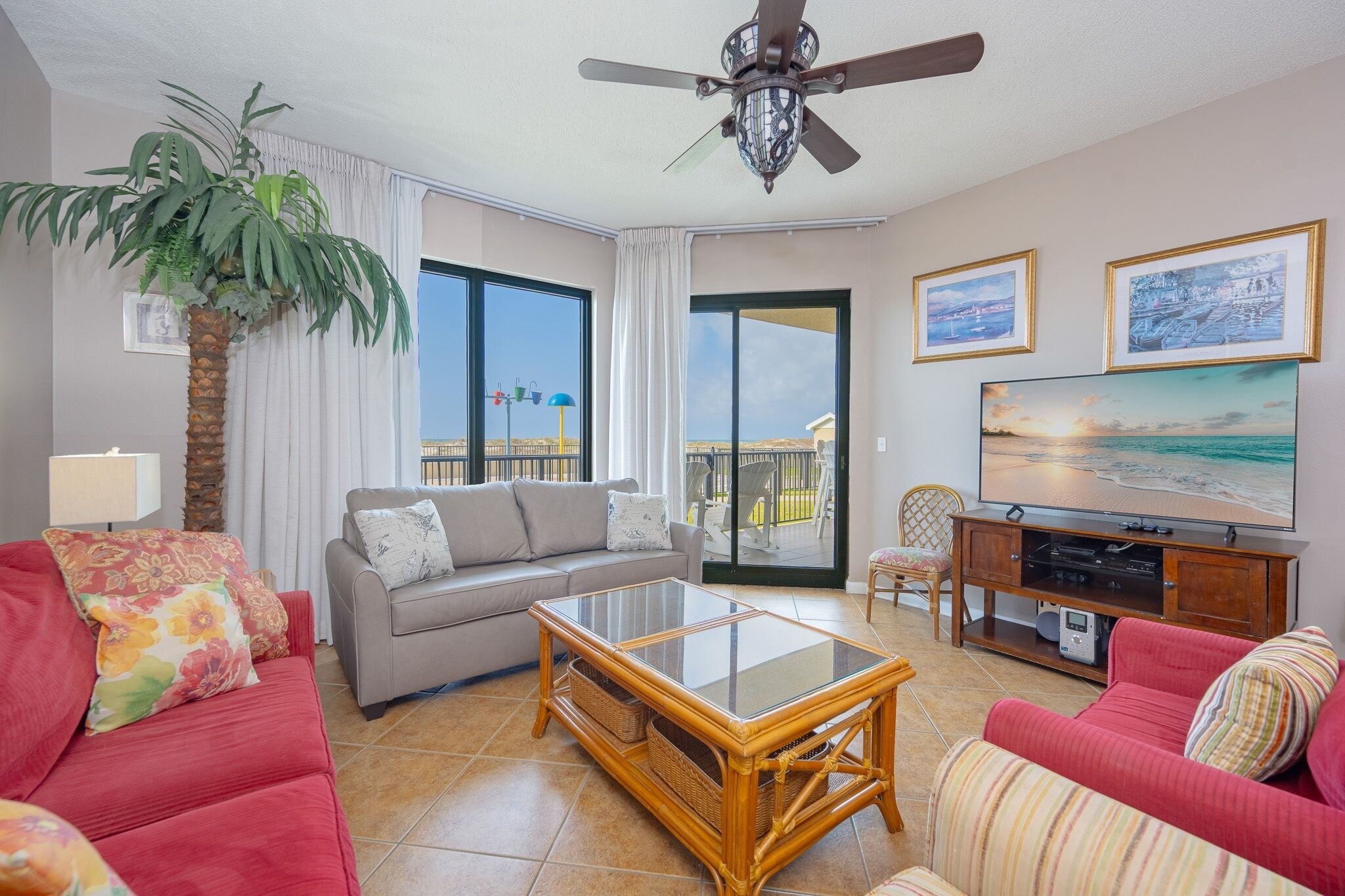 A living room with a sofa, a glass-top coffee table, a television, and a ceiling fan.
