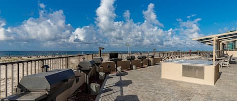 A rooftop terrace with barbecue grills, seating areas, and a view of the beach.