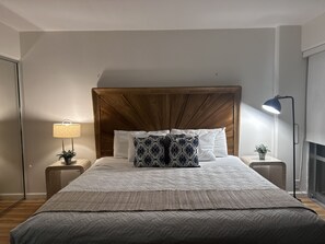 Una cama bien hecha con una colcha estampada, un cabecero de madera y una lámpara de noche.