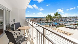 A balcony with a view of a marina and boats, a table, and two chairs. - Ilikai 1Bd 15th flr Ocean/Harbor Views-Steps to the beach! (Honolulu)