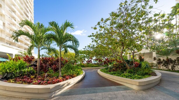 A landscaped courtyard with palm trees, a curved pathway, and a building with balconies. - Ilikai 1Bd 15th flr Ocean/Harbor Views-Steps to the beach! (Honolulu)