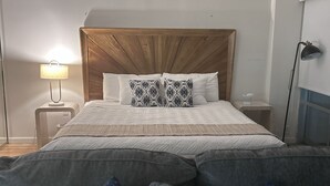 A bedroom with a wooden headboard, a bed with patterned pillows, a bedside lamp, and a nightstand. - Ilikai 1Bd 15th flr Ocean/Harbor Views-Steps to the beach! (Honolulu)