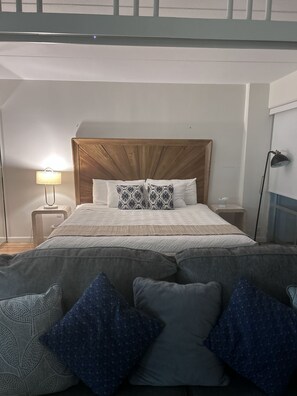 A bedroom with a wooden headboard, a bed with patterned pillows, a bedside lamp, and a nightstand. - Ilikai 1Bd 15th flr Ocean/Harbor Views-Steps to the beach! (Honolulu)