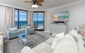 Een woonkamer met een groot raam, een plafondventilator, een flatscreen-tv en uitzicht op de oceaan.