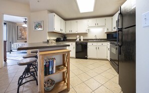 A modern kitchen with white cabinets, a black refrigerator, and a dining area with a wooden table and bar stools. - Phoenix X 307 3 Bedroom Condo (Orange Beach)
