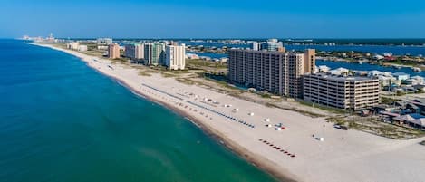 Eine Vogelperspektive einer Küstenstadt mit einem langen Sandstrand, hoch aufragenden Hotels und einem strahlend blauen Himmel.