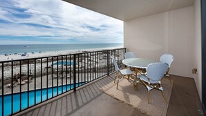 Un balcon avec vue sur la plage, une piscine et une table avec des chaises.