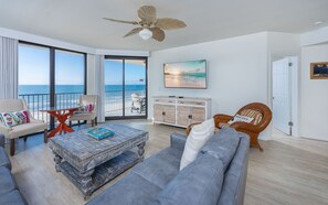 A spacious living room with a view of the ocean, a ceiling fan, and a large window. - Phoenix X 707 3 Bedroom Condo (Orange Beach)