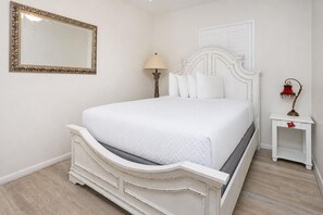 A bedroom with a bed, a nightstand, a lamp, and a mirror. - Phoenix X 707 3 Bedroom Condo (Orange Beach)