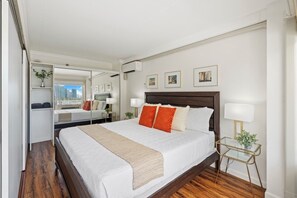Ein Hotelzimmer mit einem großen Bett, einem Nachttisch mit Lampe, einem Spiegel und Blick auf die Stadt.