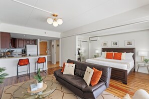 A modern hotel room with a kitchenette, a large bed, a leather sofa, and a dining area. - Ilikai 1BR Stunning Harbor/Sunset/Ocean Views! (Honolulu)