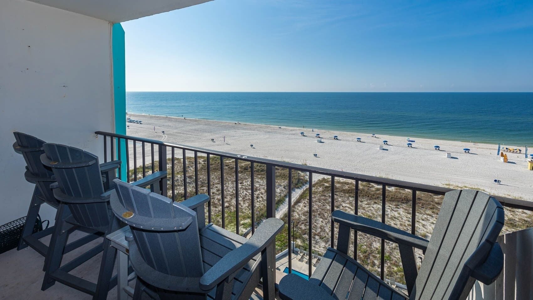 A balcony with a view of a beach, equipped with Adirondack chairs.
