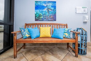 A wooden bench with patterned cushions, a wall-mounted painting of an underwater scene, and a guest parking sign. - Island Winds East 808 2 Bedroom Condo (Gulf Shores)