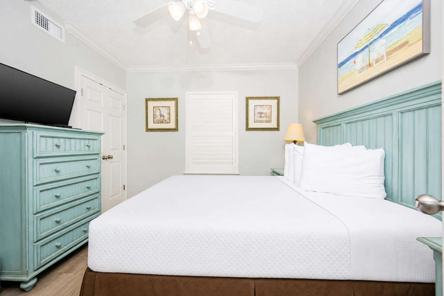 Une chambre à coucher comprenant un lit, une commode, un téléviseur et un ventilateur de plafond.