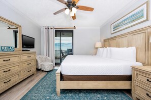Une chambre d’hôtel avec un lit, une tête de lit en bois, un téléviseur posé sur une commode, un ventilateur de plafond et une vue sur l’extérieur.
