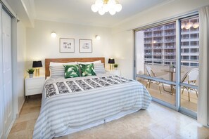 Ein Schlafzimmer mit einem Bett, Nachttischen, einem Fenster mit Blick auf ein Gebäude und einem Balkon mit Stühlen.