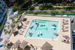 An aerial view of a rooftop pool with sun loungers and umbrellas, surrounded by greenery and buildings. - Gorgeous 2bd/2ba Ilikai Suite Steps from the Sand! (Honolulu)