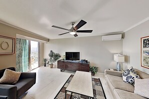 A modern living room with a ceiling fan, a flat-screen TV, a sofa, a coffee table, and a dining table. - 1BR Ocean View Luana Waikiki w/FREE PARKING! (Honolulu)