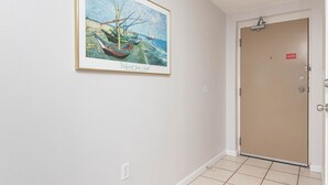 Un couloir avec un tableau encadré représentant un bateau accroché au mur, une porte dotée d’une serrure et un luminaire au plafond.