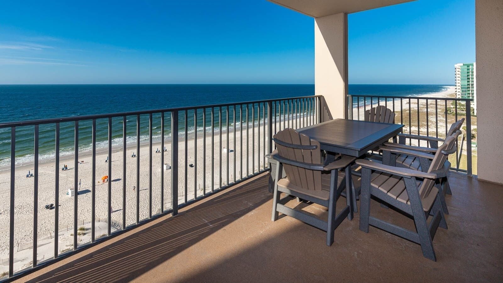 A balcony with a view of the beach and ocean, a table, and chairs.