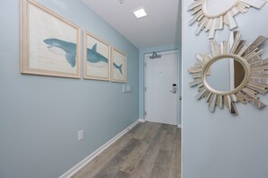 A hallway with light blue walls, wooden flooring, and three framed shark paintings. - Phoenix X 513 3 Bedroom Condo (Orange Beach)