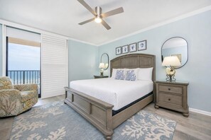 Une chambre à coucher avec un lit, des tables de chevet, un ventilateur de plafond, une chaise et une vue sur l’océan.