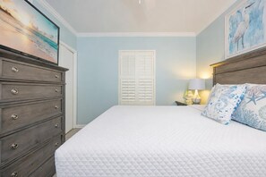 A bedroom with a bed, a dresser, a nightstand with a lamp, and a door with shutters. - Phoenix X 513 3 Bedroom Condo (Orange Beach)