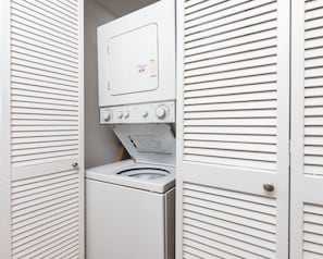 A compact, white laundry room with a front-loading washing machine and a dryer. - Island Winds East 107 2 Bedroom Condo (Gulf Shores)