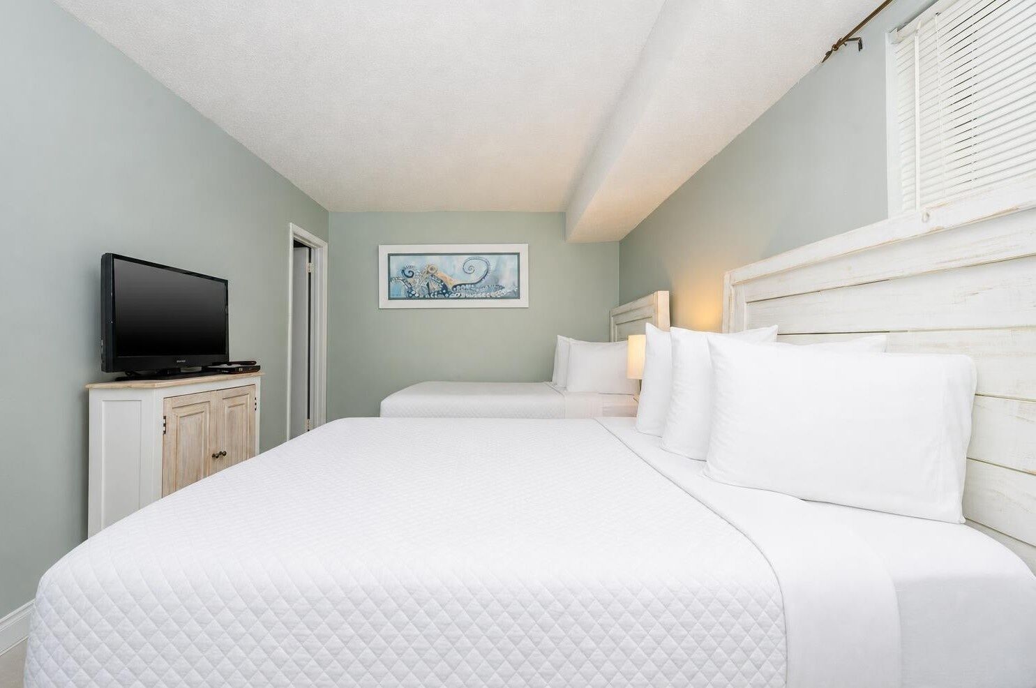 A hotel room with a bed, a television on a cabinet, and a painting on the wall.