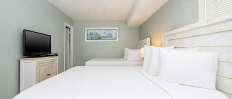 Una habitación de hotel con una cama, un televisor sobre una mesita y un cuadro en la pared.