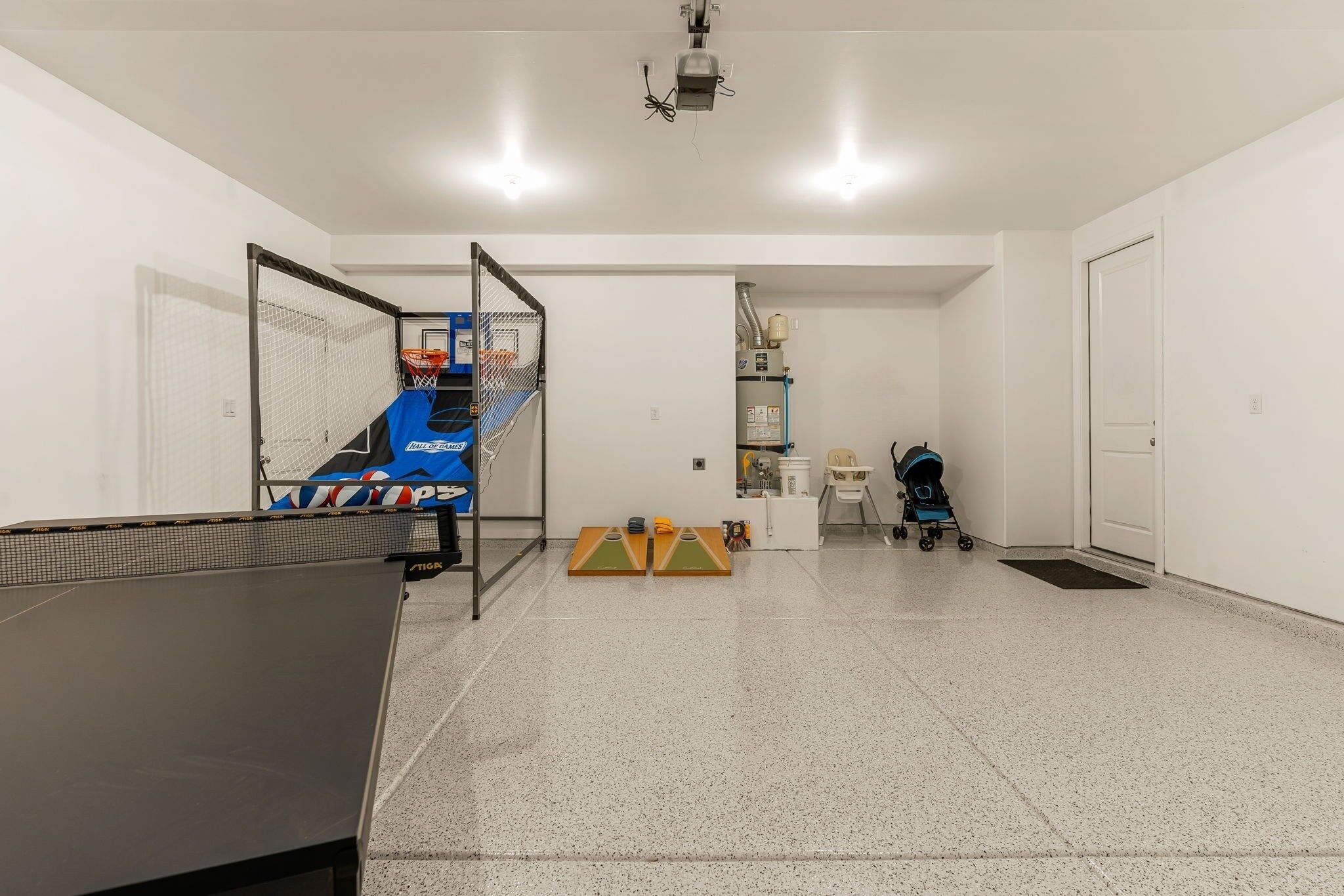 A spacious room with a ping pong table, a basketball hoop, and a baby stroller.