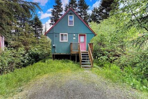 A small, single-story cabin with a red door and a wooden staircase leading to a deck. - Quiet A-frame Tucked Off the Road in Girdwood (Girdwood)