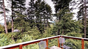 A wooden deck with two chairs and a table, surrounded by dense forest and tall trees. - Quiet A-frame Tucked Off the Road in Girdwood (Girdwood)