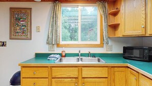 A kitchen with wooden cabinets, a sink, and a microwave. - Quiet A-frame Tucked Off the Road in Girdwood (Girdwood)