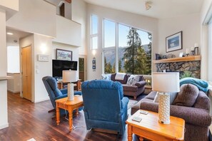 Ein großzügiges Wohnzimmer mit Kamin, bequemen Sitzmöglichkeiten und einem großen Fenster mit Blick auf die Berge.