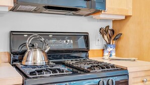 Una cocina con estufa, hervidor y utensilios.
