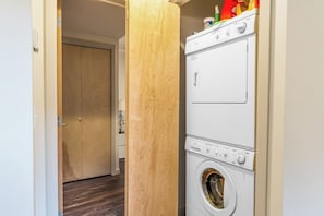 Un lavadero con lavadoras y secadoras apiladas, una puerta de madera y un piso de madera oscura.