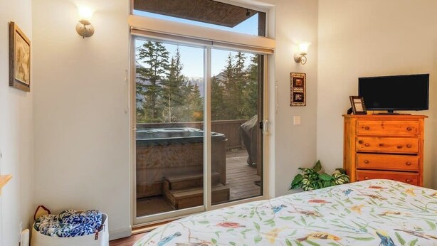 Un dormitorio con cama, cómoda, televisor y puerta corrediza de vidrio que da a un balcón.